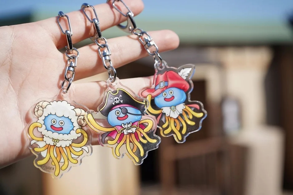 手で持たれた、可愛らしいドラゴンクエストのスライム型キーホルダーが3つ写っています。羊、海賊、魔法使いのような衣装をまとった個性豊かなデザインが特徴的です。