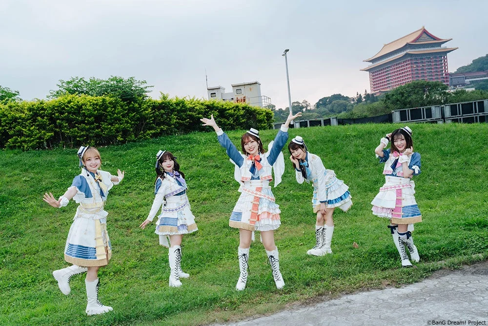 カラフルな衣装を着た5人の女性が、屋外の芝生で笑顔でポーズをとっています